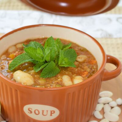 Bean and lentil soup in a terracotta bowl, topped with fresh mint
