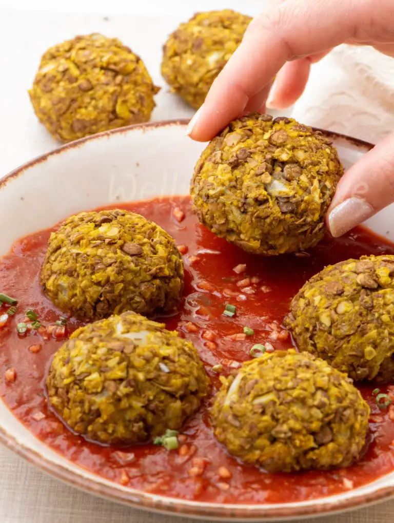 Vegan meatballs in a plate with a hand taking a meatballs