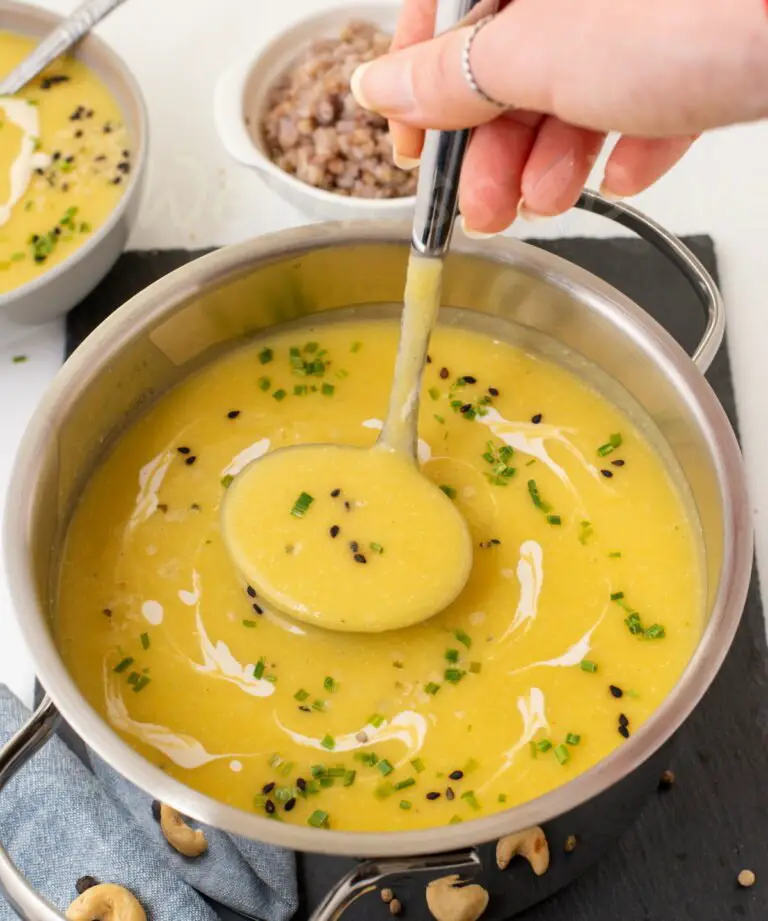 creamy zucchini soup in a pot, with a hand taking some with ladle
