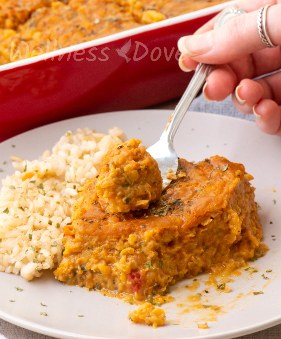a piece of the vegan casserole on a plate. A hand is taking a piece with a fork.