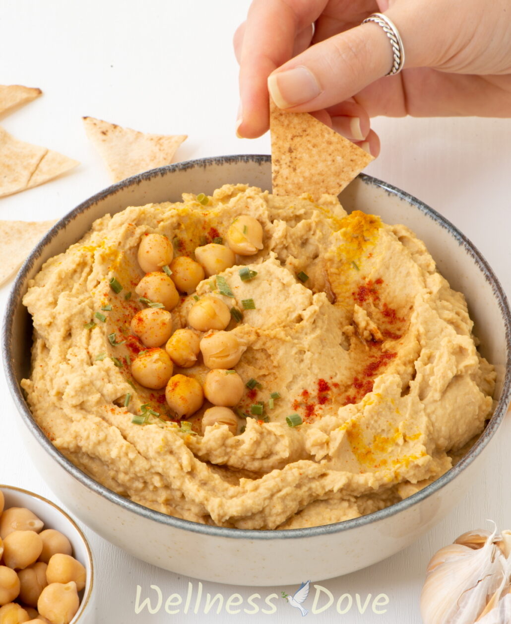 3/4 view of the 5 ingredient oil-free vegan hummus with a hand taking a bite with a cracker