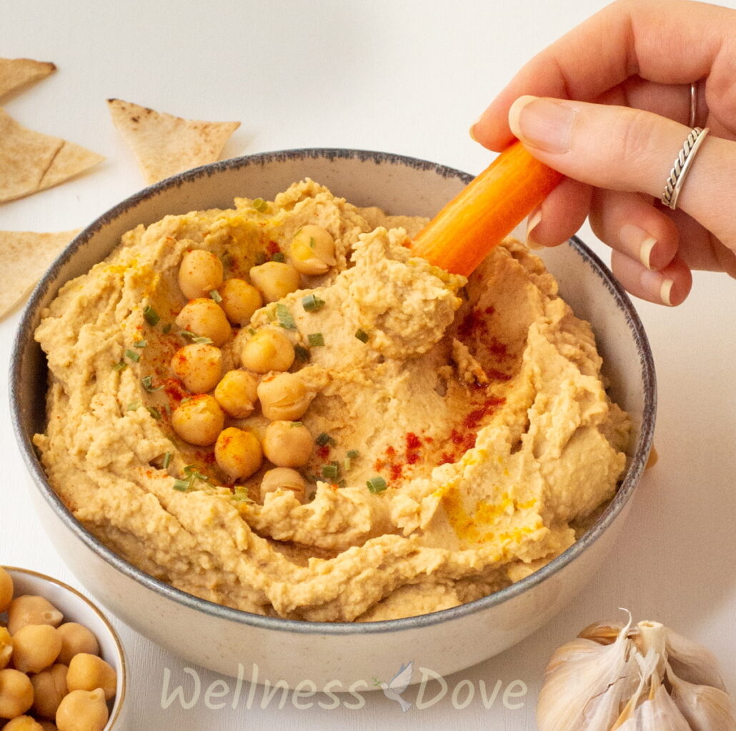 a hand taking some of the 5 ingredient oil-free vegan hummus with a carrot