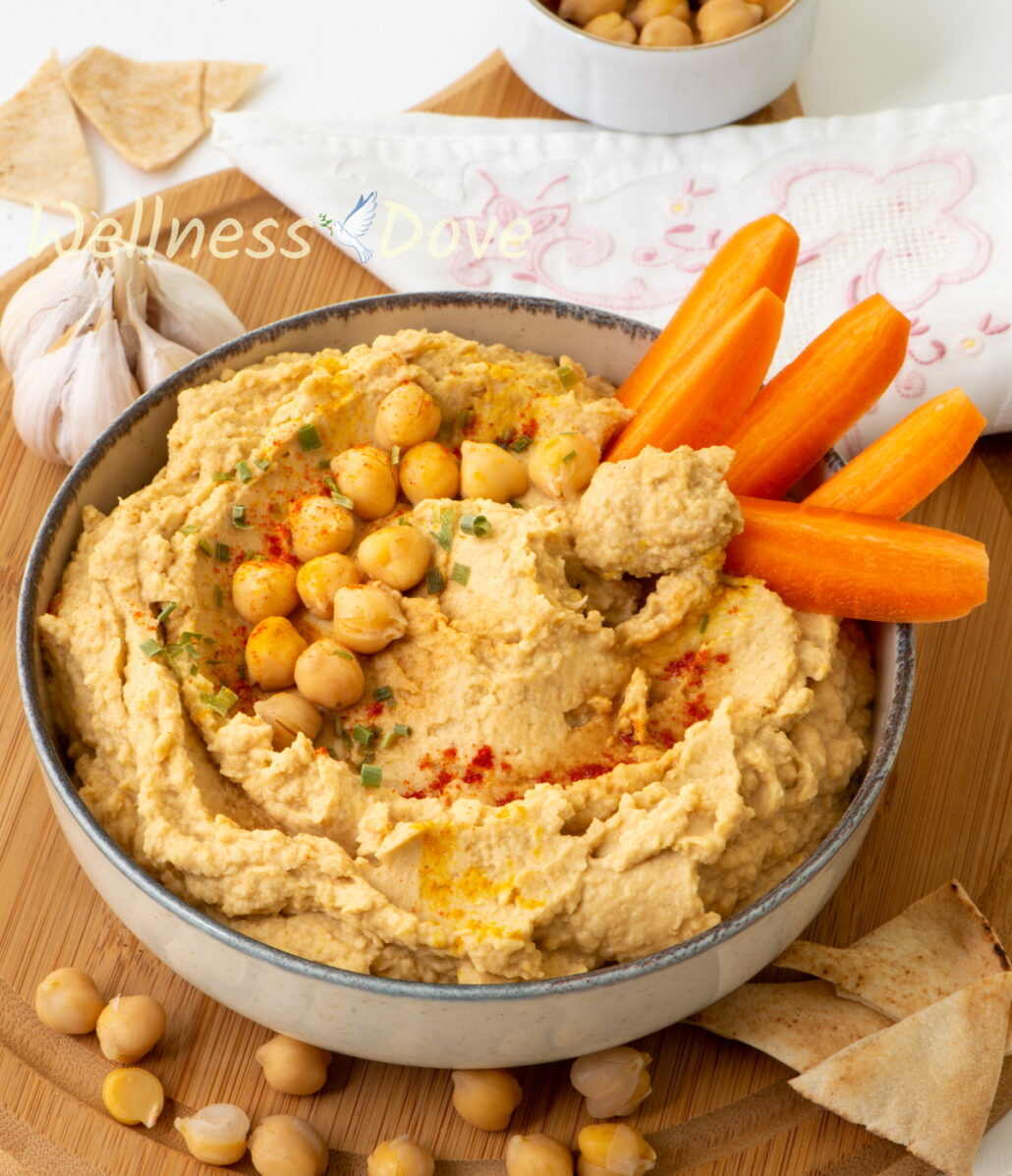 the 5 ingredient oil-free vegan hummus in a bowl on a chopping board with carrot sticked in it