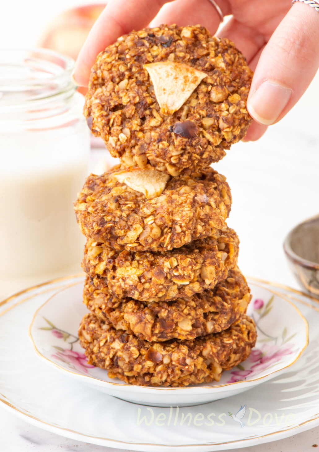 Apple Oatmeal Vegan Breakfast Cookies stacked on top of each other and a hand is taking the top cookie away.