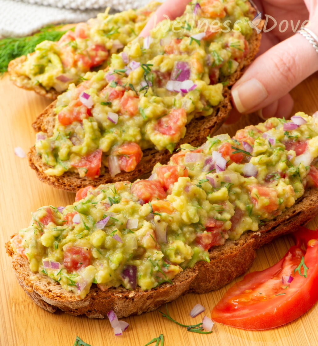 the vegan homemade guacamole spread over sandwiches and a hand is taking a sandwich 