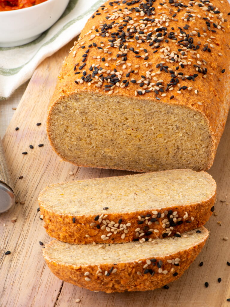 Loaf of red lentil bread topped with sesame seeds, with two slices cut