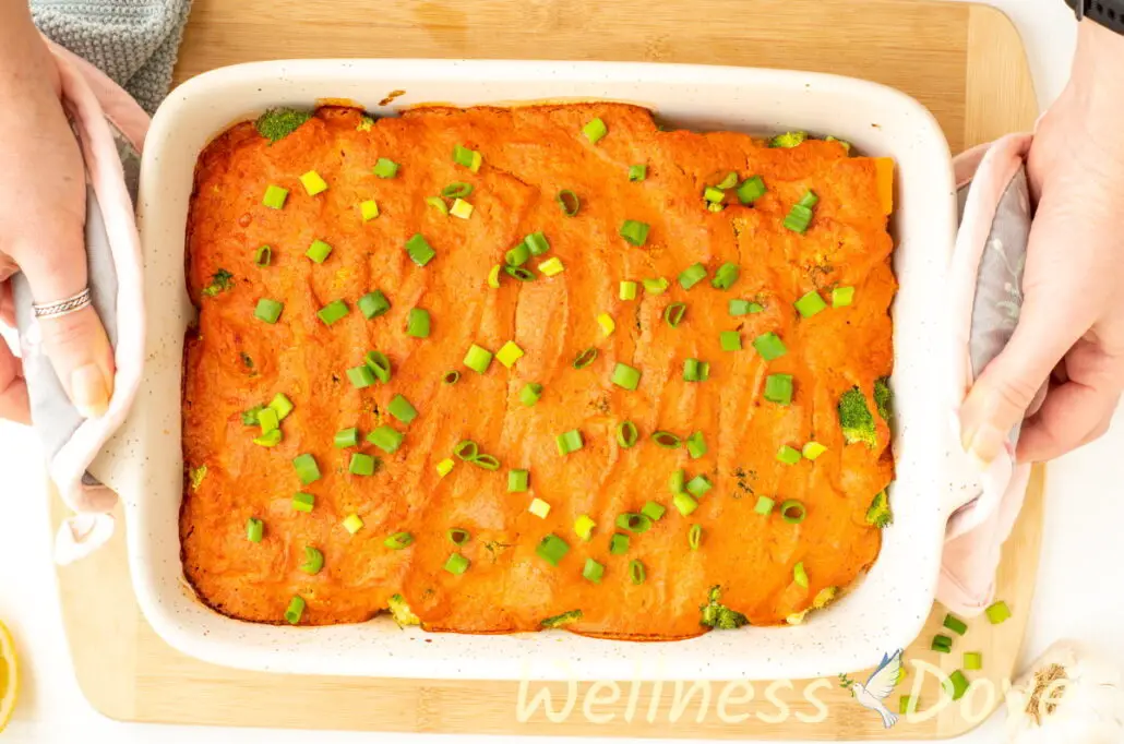 an overhead photo of the  vegan broccoli casserole while two hands are serving it over a board