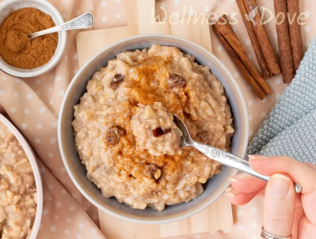 an overhead view of the  quick vegan brown rice pudding in a bowl and a hand is taking some of it out with a spoon