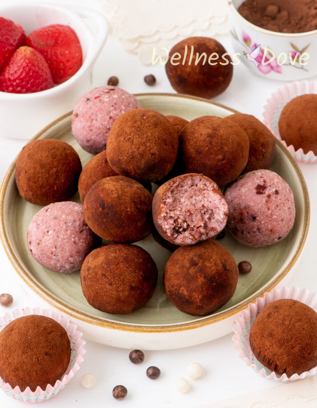 a /34 view of the strawberry vegan truffles i a small plate, one of the strawberry vegan truffles has half of it bitten off