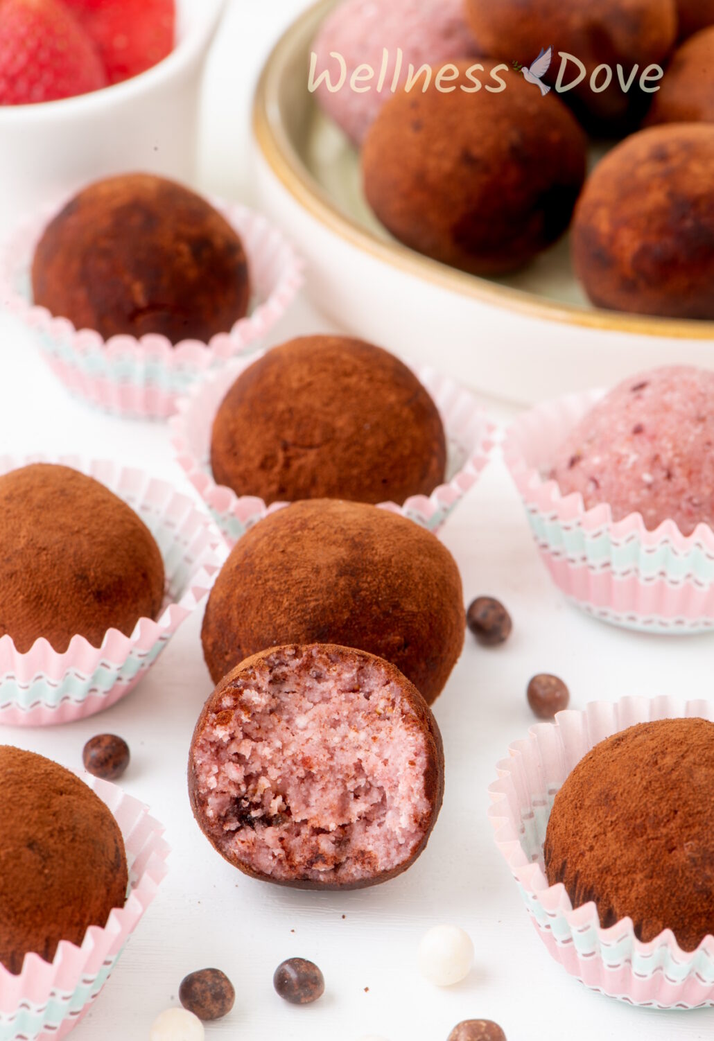 a couple of the strawberry vegan truffles on a table, a half of one of hem is bitten off