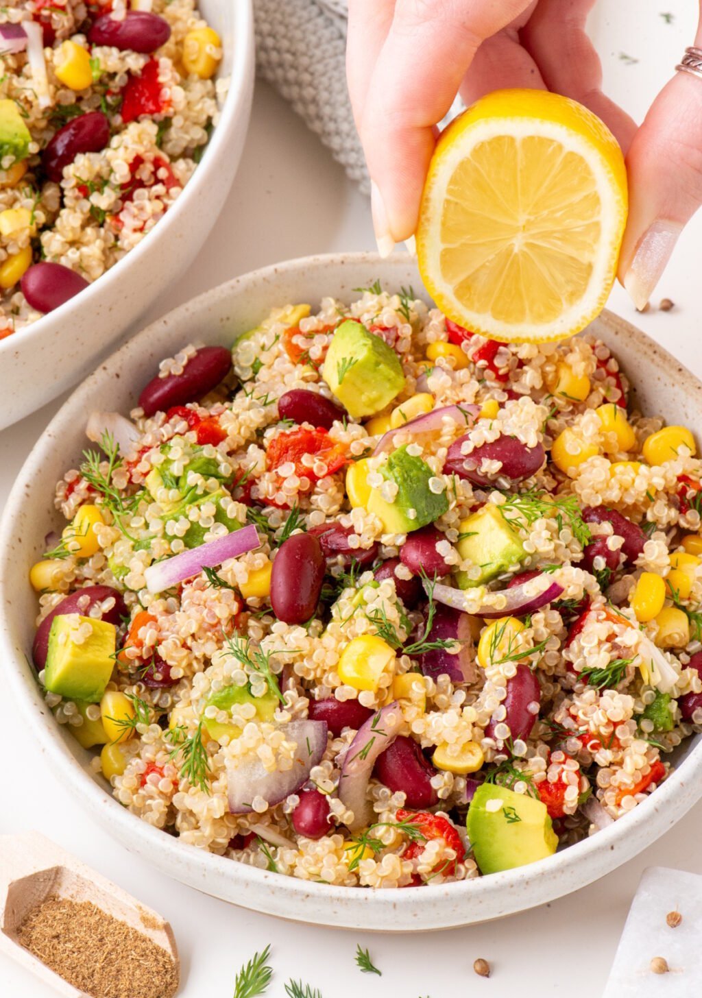 the vegan avocado quinoa salad in a small bowl and a hand is squirting some lemon on it