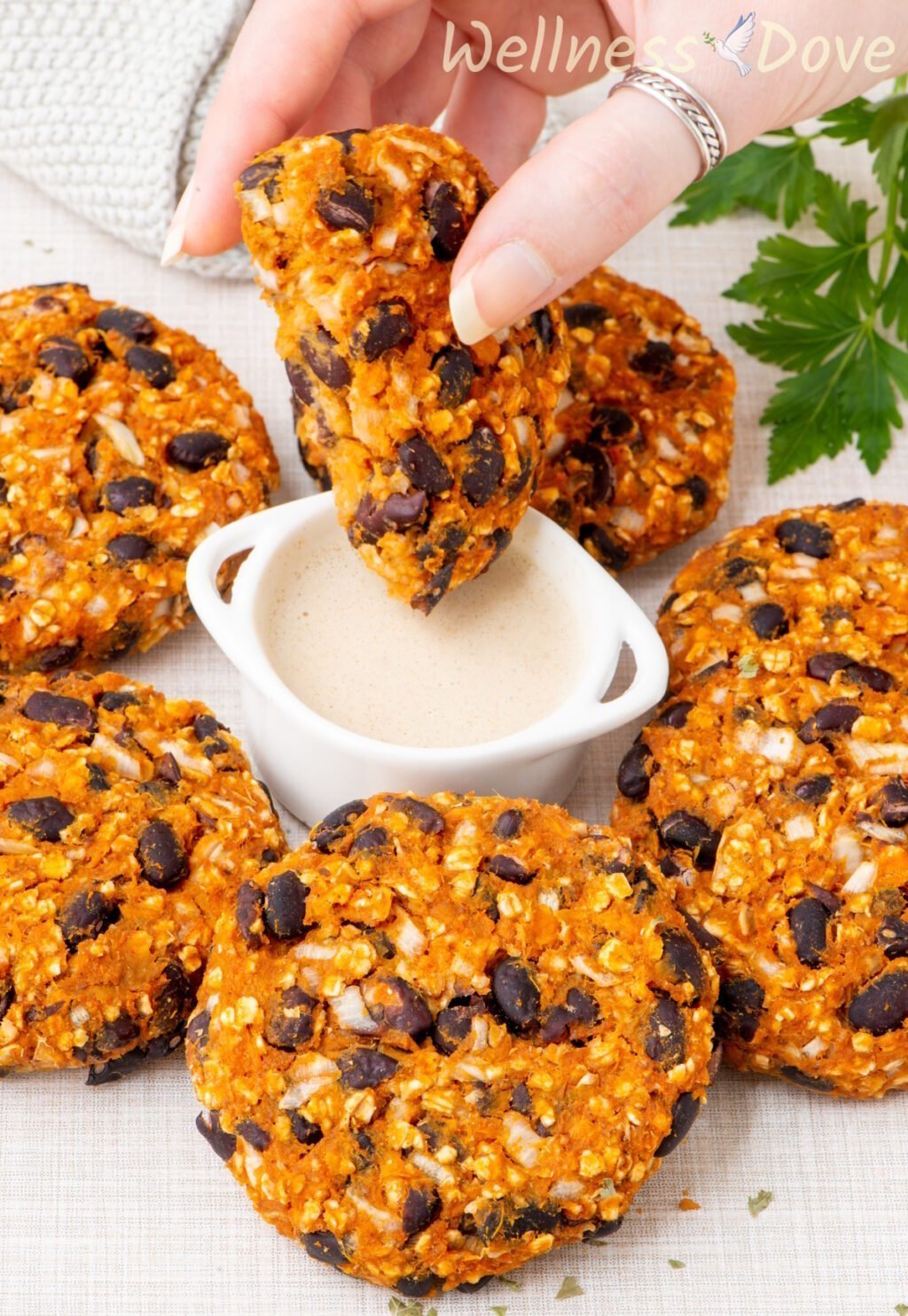 a hand is dipping one of the Sweet Potato Black Bean Burgers in some sauce. 