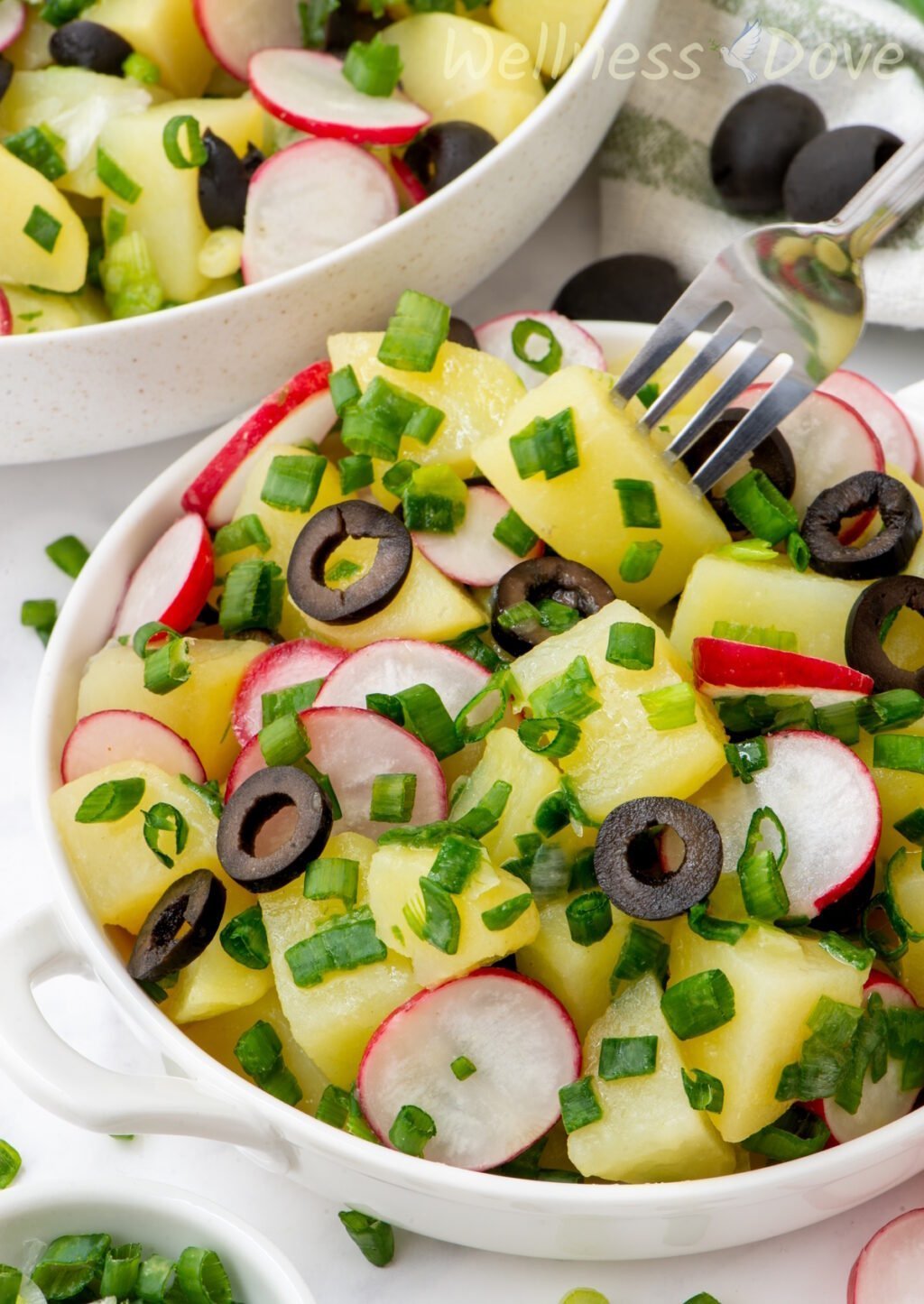 the vegan no mayo potato salad in a  small bowl and a fork is taking a potato out