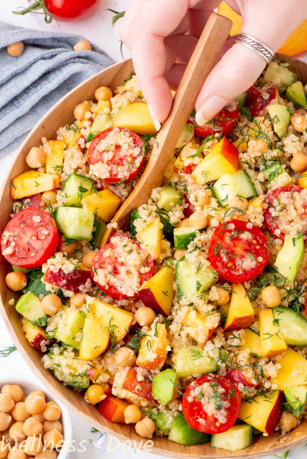 a macro shot of the chickpea quinoa vegan salad while a hand is tossing it with a wooden spoon