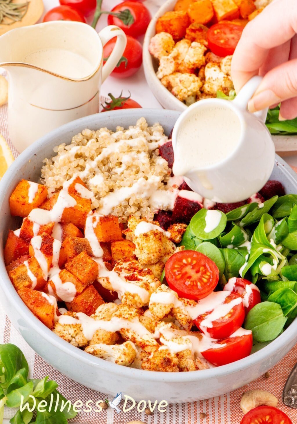 the Roasted Cauliflower Quinoa Beet Bowl photographed from a 3/4 angled while a hand is pouring some sauce over the bowl