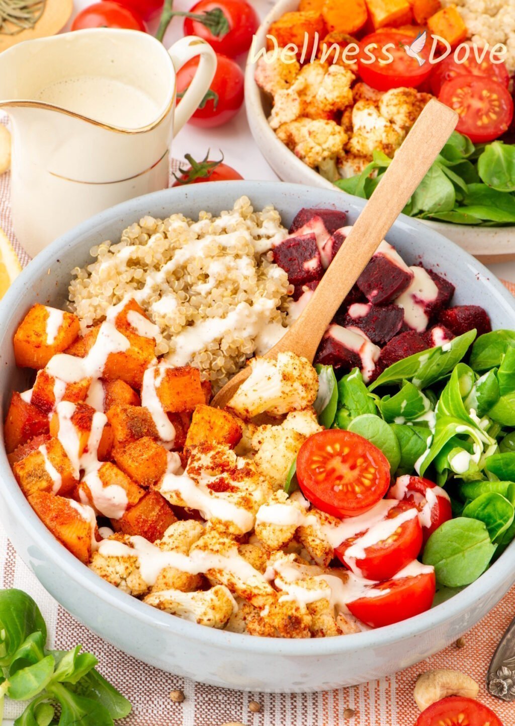 the Roasted Cauliflower Quinoa Beet Bowl with sauce poured over it and a spoon is stuck in the bowl