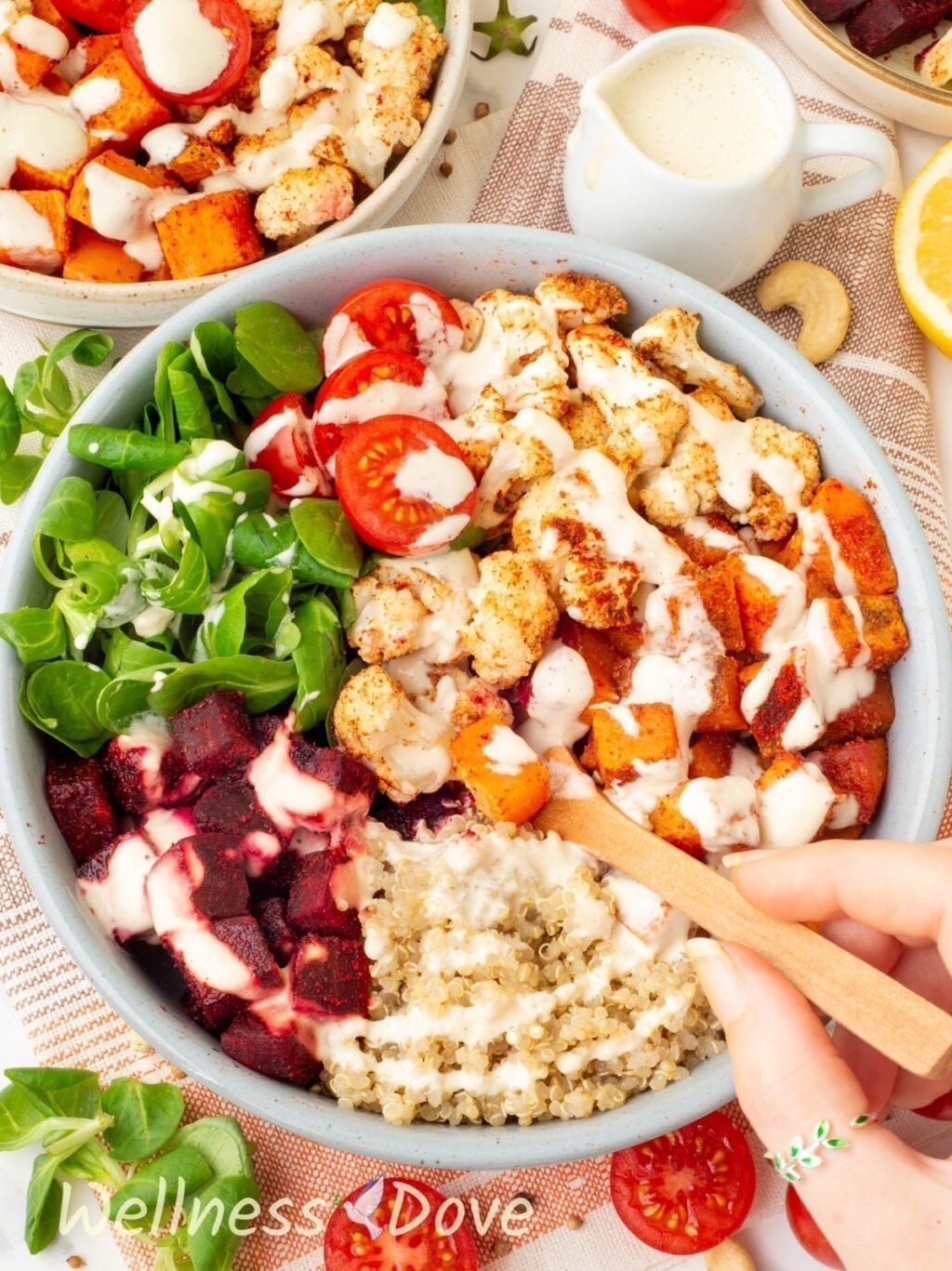 the Roasted Cauliflower Quinoa Beet Bowl with sauce poured over it and a hand is taking some of the food with a spoon