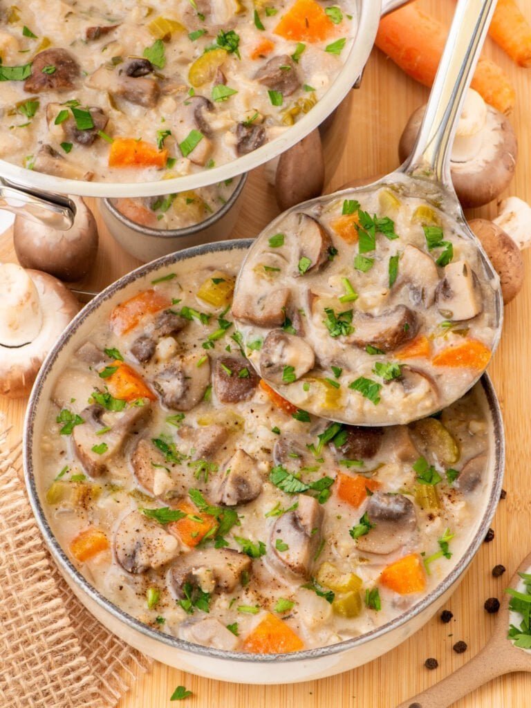Creamy mushroom soup with carrots and herbs in a pot, with a ladle
