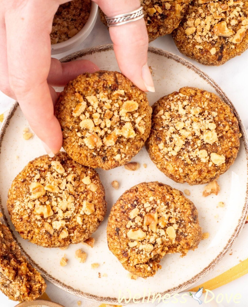 the Easy Oatmeal Walnut Vegan Cookies in a small plate and a hand is taking a cookie out