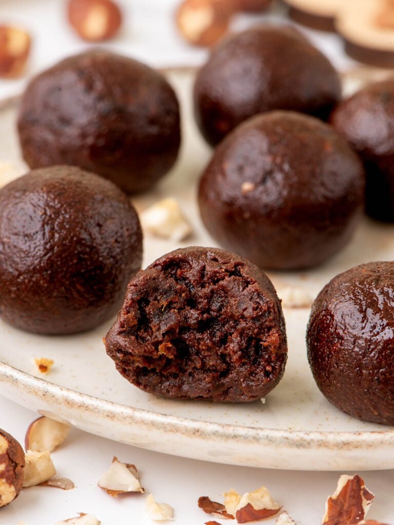 Chocolate date energy balls on a plate, one cut open to show the inside